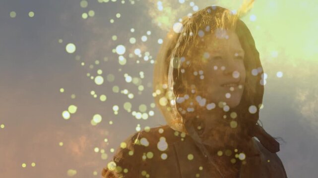Hooded woman turning to sun as golden bokeh drifting over face revealing gentle smile, marketing