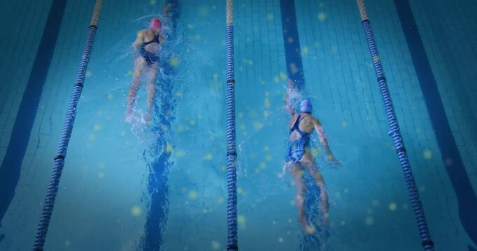 Top-down tracking two women swimmers training backstroke in pool, light flecks glinting on splashes