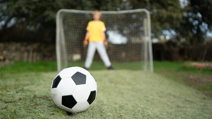 Obraz premium Soccer ball on grass with kid preparing to defend goal