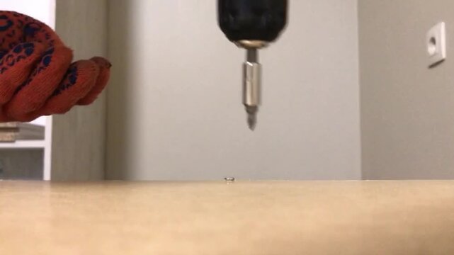 A screwdriver screws a screw into the beige surface of a cabinet