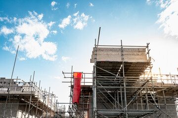 Dramatic view of early evening scaffolding seen on a new housing development in the UK. The sun is seen setting behind some of the scaffolding poles.