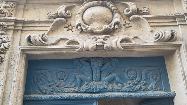 Decorative carved stone lintel with ornamental relief above a blue doorway on a historic facade in Montpellier, France