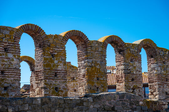 Side-view of the iconic red brick and stone arches of the Church of Saint Sophia ruins in Nesebar, Bulgaria, standing against a vibrant blue sky.