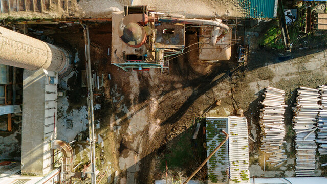 Aerial view of the old industrial complex, where rust-colored buildings meet weathered concrete, casting dark shadows across the cracked ground, Sremska Mitrovica, Vojvodina, Serbia.