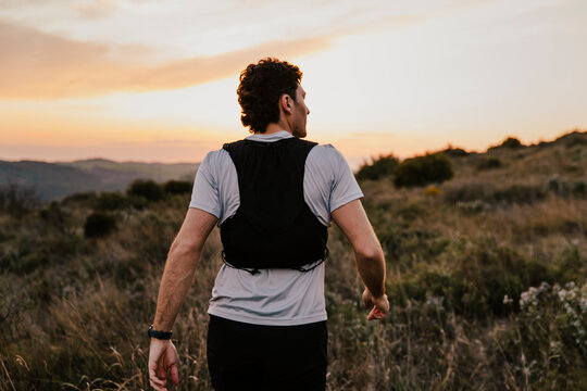 Male trail runner standing in a natural meadow surrounded by grass while observing the landscape before continuing his training run. Concept of outdoor adventure.