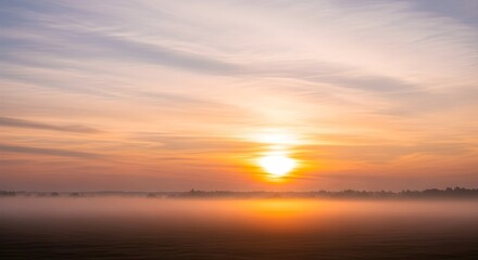 Fototapeta premium Vibrant sunrise over a misty field with golden light and atmospheric clouds