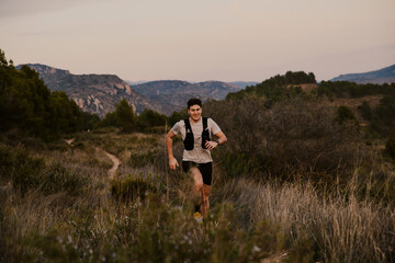 Male endurance runner running along a narrow mountain trail surrounded by natural vegetation. Outdoor sports concept focused on trail running, adventure and fitness.