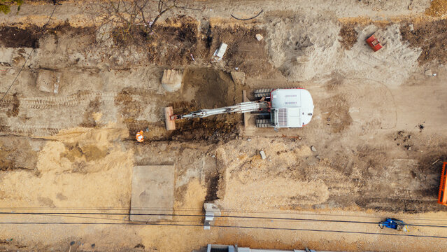 Aerial view of a construction site with an excavator digging into the earth, surrounded by piles of dirt and raw materials, Belgrade, City of Belgrade, Serbia.