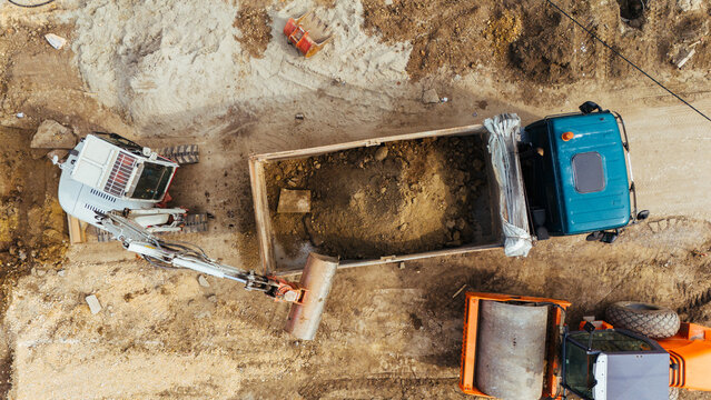 Aerial view of an excavator, a truck, and other construction equipment, contrasting the beige earth with the turquoise truck and orange elements, Belgrade, City of Belgrade, Serbia.