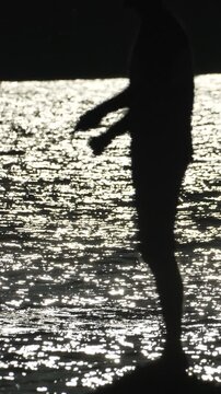 Fishing silhouette water, person casting line against sparkling sun reflection at sunset. Vertical video