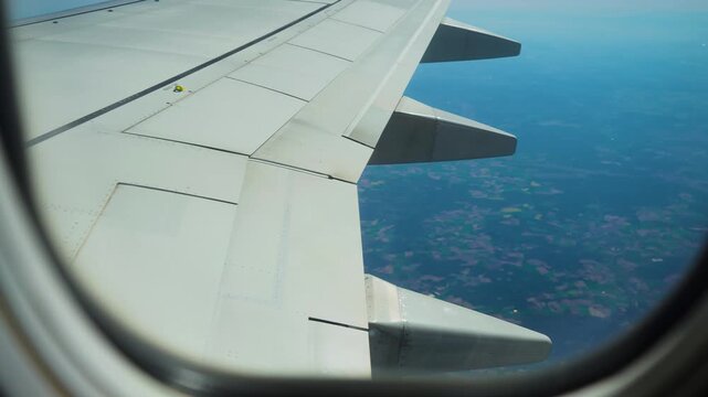 Airplane flying above scattered farmland with dense forest areas, view from window porthole. Jet cruising over patchy countryside in bright daylight. Aircraft gliding above varied terrain with fields