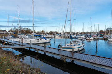 Fototapeta premium Ishoj Marina, Denmark – November 17, 2025: Large marina filled with sailboats and motor yachts moored along floating wooden piers. Tall masts rise above the harbor creating a dense pattern against the