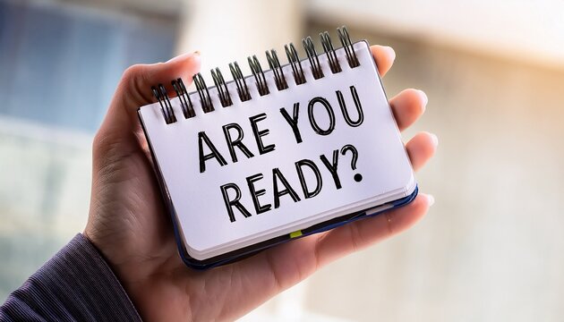 are you ready a close up shot of a hand holding a notepad featuring the words are you ready in bold eye catching text the image s soft diffused background adds depth