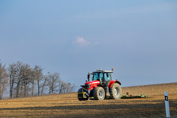 Obraz premium Red tractor plowing field in Hlina, Jihomoravsky kraj