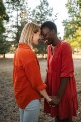 Fototapeta premium Two Smiling Women Holding Hands and Touching Foreheads in a Park