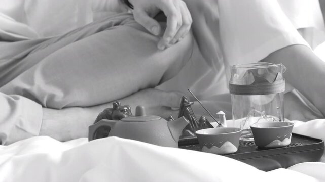 Tea set with glass teapot on tray beside person sitting on bed