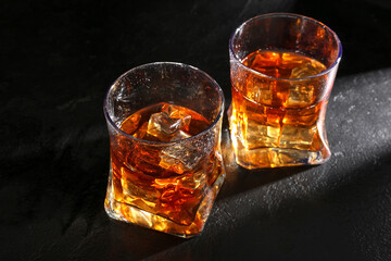 Glasses of whiskey with ice cubes on dark background