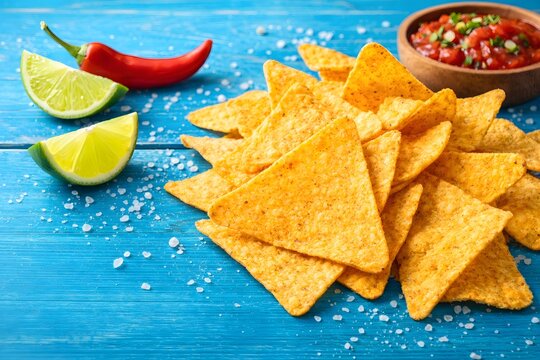 Traditional mexican appetizers. Corn nachos with lime, cilantro and spicy sauce on rustic wooden surface.
