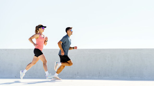 Active man and woman jogging side by side outdoors on a bright day with a clean background