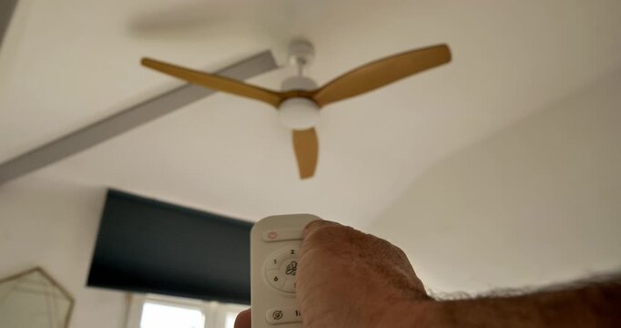 Ceiling Fan Control: A hand aims a remote at a sleek ceiling fan, the blurred motion of the blades hinting at the refreshing breeze. The image encapsulates comfort and technology integration.