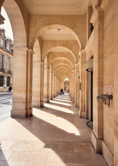 Obraz premium Walking under a sunlit arcade in Paris, France. 
