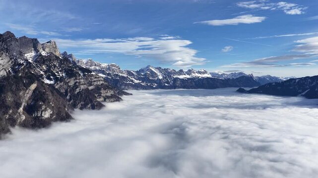Aerial panorama above Walensee Lake covered by a vast sea of clouds with dramatic alpine peaks rising above the fog. Cinematic Swiss winter landscape. Concept of freedom and untouched nature.