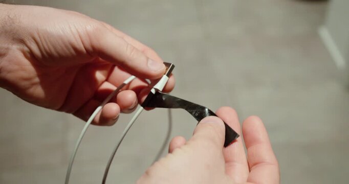 Close-up of hands showing a damaged charging cable with broken insulation. Concept of electrical safety, faulty electronics, cable wear, and device charging problems.