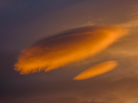Two lenticular clouds glow orange against a dusky sky. Adamello Brenta Natural Park,Madonna di Campiglio,Trentino,Italy