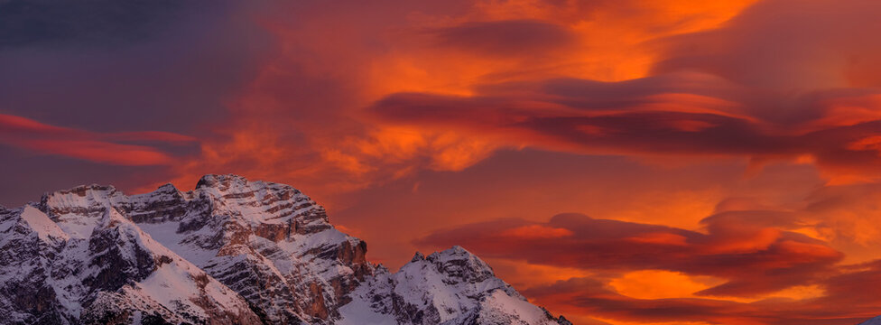 Snow-covered Brenta mountain peaks are silhouetted against a vibrant, fiery sunset sky filled with orange and red clouds. Adamello Brenta Natural Park,Madonna di Campiglio,Trentino,Italy
