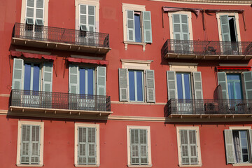 Obraz premium A classic Mediterranean-style building with red ochre walls, windows, and balconies with decorative wrought-iron railings. A typical façade of an old French residential building