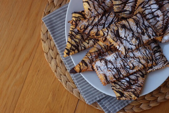 Italian sweet crisp pastry deep-fried and sprinkled with dark chocolate on wooden table. Chiacchere or crostoli, bugie, cenci 