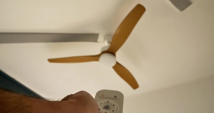 Ceiling Fan Operation: A modern ceiling fan with wooden blades is controlled using a remote, offering a blend of functionality and design.