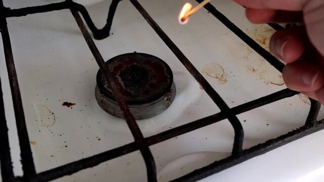 A man lights a gas burner on an old stove with a match
