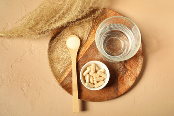 Fototapeta premium Spoon with collagen powder, pills and glass of water on beige grunge background