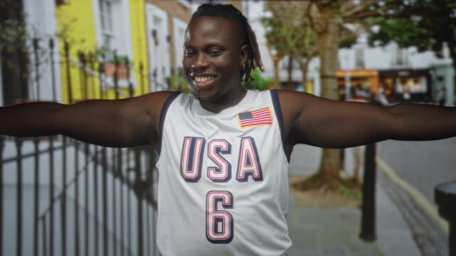 Man with bare arms outstretched on street wearing usa basketball jersey with flag patch, smiling broadly and looking upward; joy freedom.