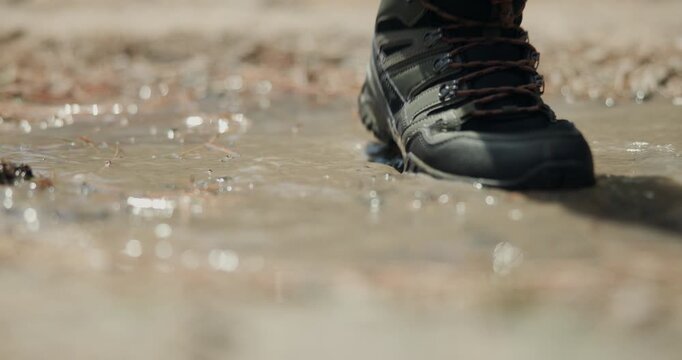 Person, shoes and hiking with muddy puddle on trail or path for journey or outdoor adventure. Closeup, sneakers or hikers walking with boots or water splash for travel, trekking or trip on dirt road