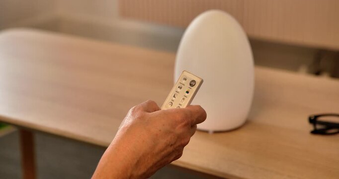 Morning Ritual: A hand, wielding a remote, prepares to adjust a futuristic egg-shaped light on a wooden surface, embodying the dawn of a new day.
