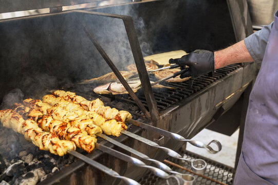 Chef working at a large metal barbecue with various food piece grilling on fire.