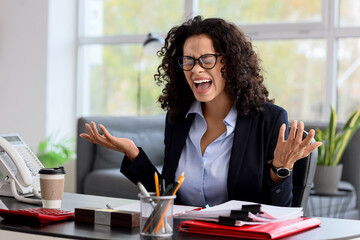 Angry African-American businesswoman at desk in office