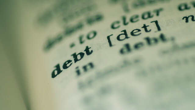 Extreme close-up of the word debt and its definition printed in an old dictionary page. Macro shot with selective focus on financial vocabulary, money problem, credit, bankruptcy, macroeconomic