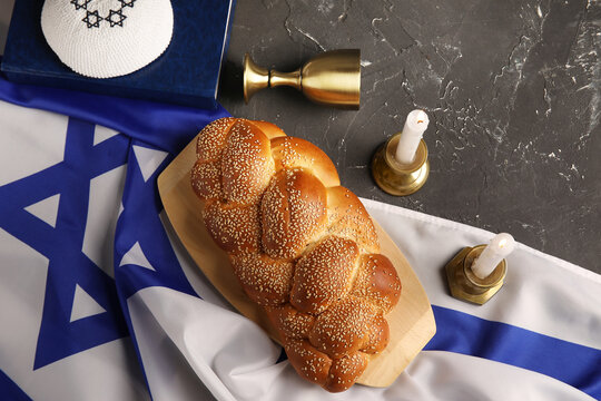 Traditional challah bread with flag of Israel, wine goblet, kipa and burning candles on grey grunge table. Shabbat Shalom