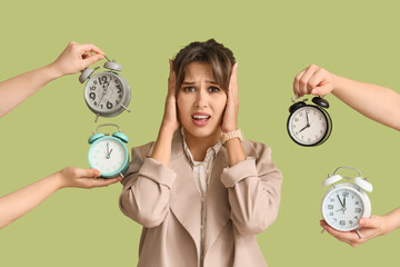 Shocked young businesswoman surrounded by hands with alarm clocks on green background. Deadline...