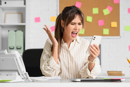 Screaming young businesswoman with mobile phone at her workspace in office