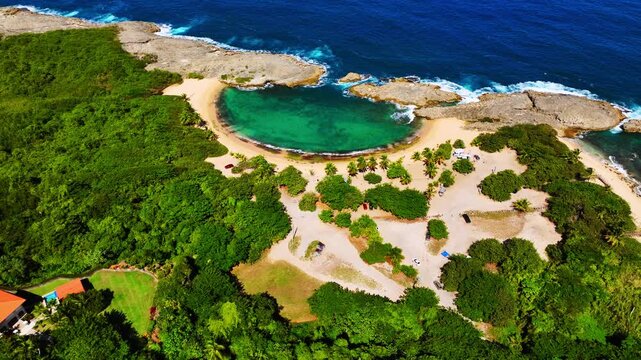 Natural limestone cove with turquoise water and sandy beach surrounded by green vegetation and palm trees. Aerial view of Mar Chiquita beach in Manati Puerto Rico.