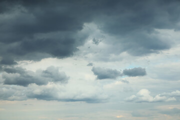 Obraz premium Dramatic dark storm clouds over pale blue sky with layered overcast atmosphere and moody weather background