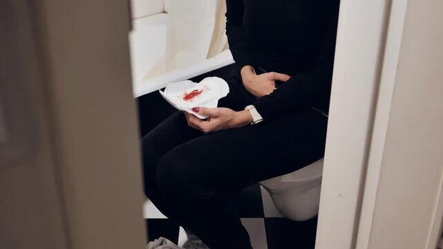 Woman sitting in bathroom holding blood stained sanitary pad during period pain