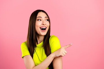 Young woman smiling and pointing to the right on pink background with vibrant neon top, excited...
