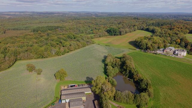 Slow high flight over farm,large country house pond and green fields on the edge of the Bere Forest Rookesbury Park,Wickham,Hampshire in bright early Autumn sunlight with colourful trees