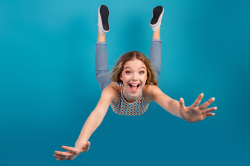 Young girl in mid air smiling wide as she flies with arms outstretched against blue background