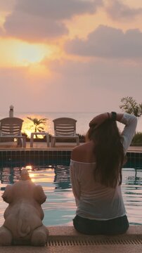 Tranquil beach resort with palm trees, calm ocean, and breathtaking sunset. Luxury spa swimming pool. Long hair caucasian brunette enjoy colorful sky and sea ocean scene. Back view, slow motion